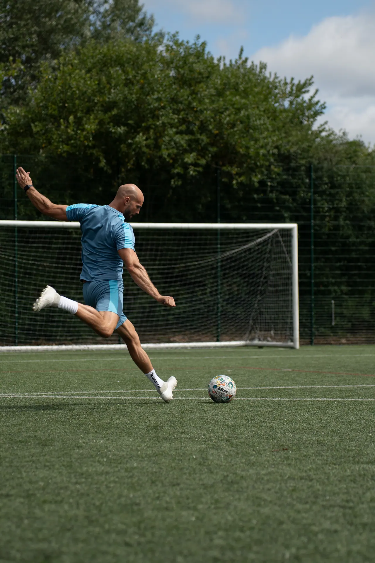 Daniel striking a football on a pitch